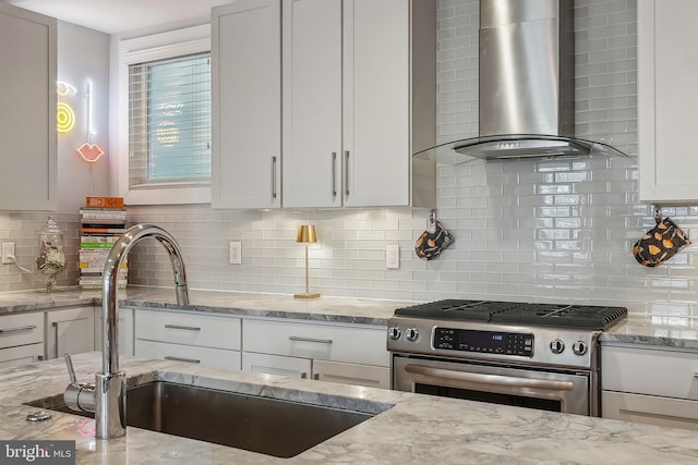 kitchen with wall chimney exhaust hood, light stone countertops, gas range, and white cabinets