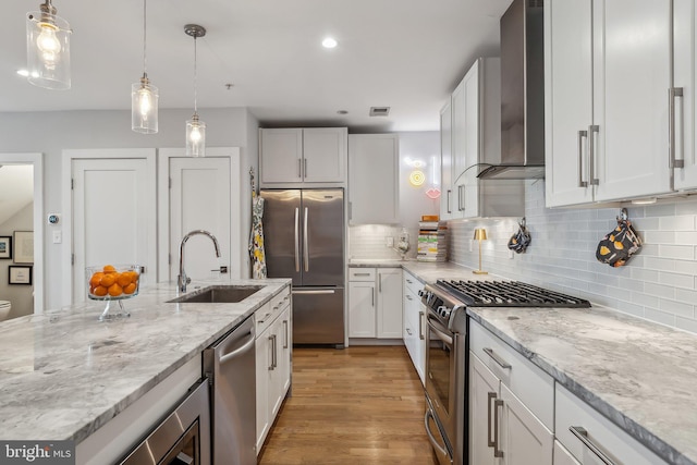 kitchen featuring stainless steel appliances, a sink, white cabinetry, wall chimney range hood, and pendant lighting