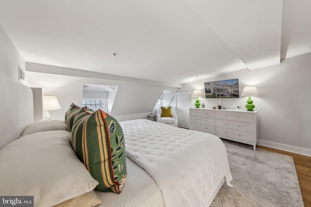 bedroom with lofted ceiling, baseboards, visible vents, and light wood finished floors