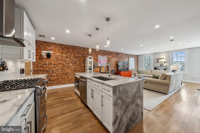 kitchen with stainless steel appliances, white cabinetry, a sink, and wall chimney range hood