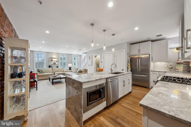 kitchen featuring light stone counters, a center island with sink, appliances with stainless steel finishes, white cabinets, and a sink