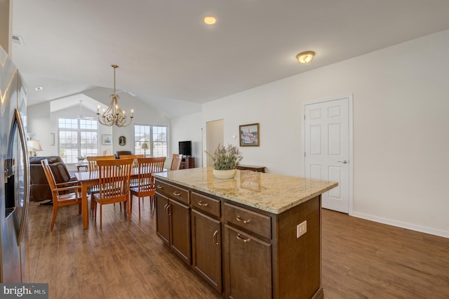 kitchen featuring light stone countertops, vaulted ceiling, a chandelier, a center island, and hanging light fixtures