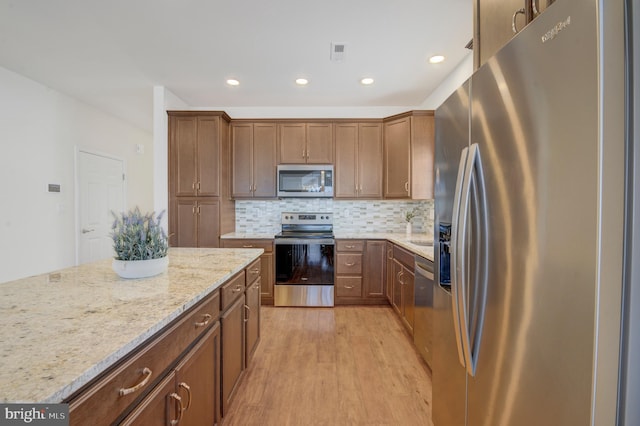 kitchen featuring tasteful backsplash, light stone countertops, light hardwood / wood-style floors, and appliances with stainless steel finishes