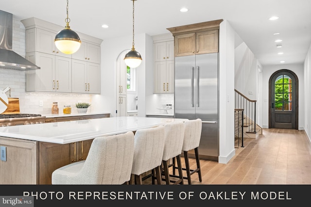 kitchen with stainless steel built in fridge, a kitchen island, light hardwood / wood-style flooring, wall chimney range hood, and tasteful backsplash