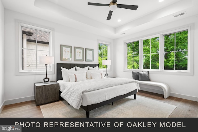 bedroom featuring a raised ceiling, ceiling fan, and light hardwood / wood-style flooring