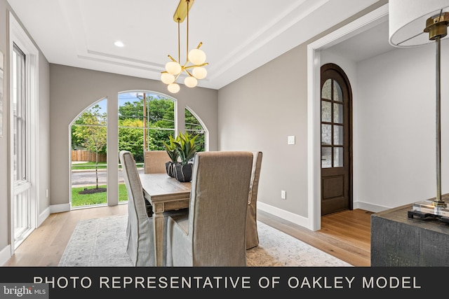 dining space with light hardwood / wood-style floors, an inviting chandelier, and a tray ceiling