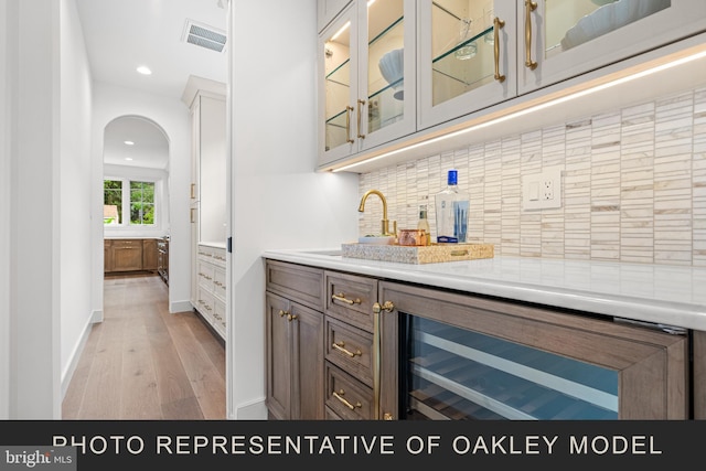 bar featuring light hardwood / wood-style floors, beverage cooler, sink, and decorative backsplash