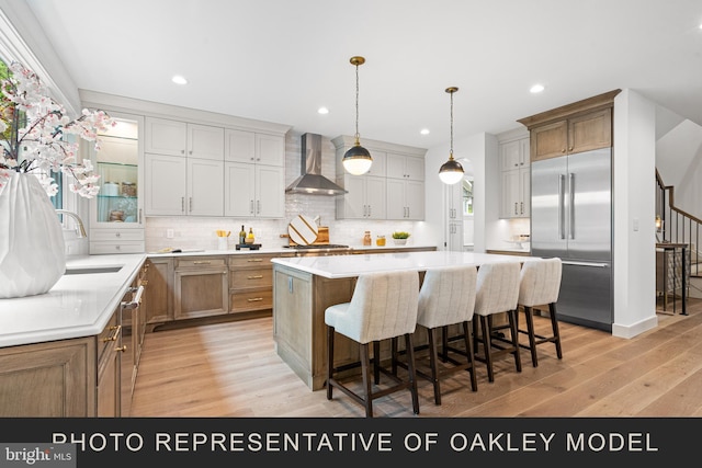 kitchen with stainless steel built in refrigerator, a large island, wall chimney exhaust hood, light hardwood / wood-style floors, and hanging light fixtures