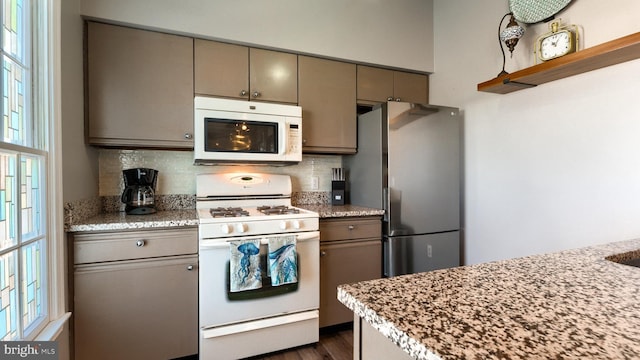 kitchen with light stone counters, white appliances, backsplash, and dark wood-type flooring