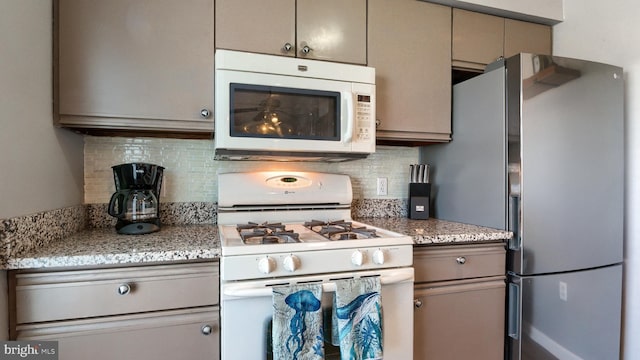 kitchen with backsplash, gray cabinetry, light stone countertops, and white appliances