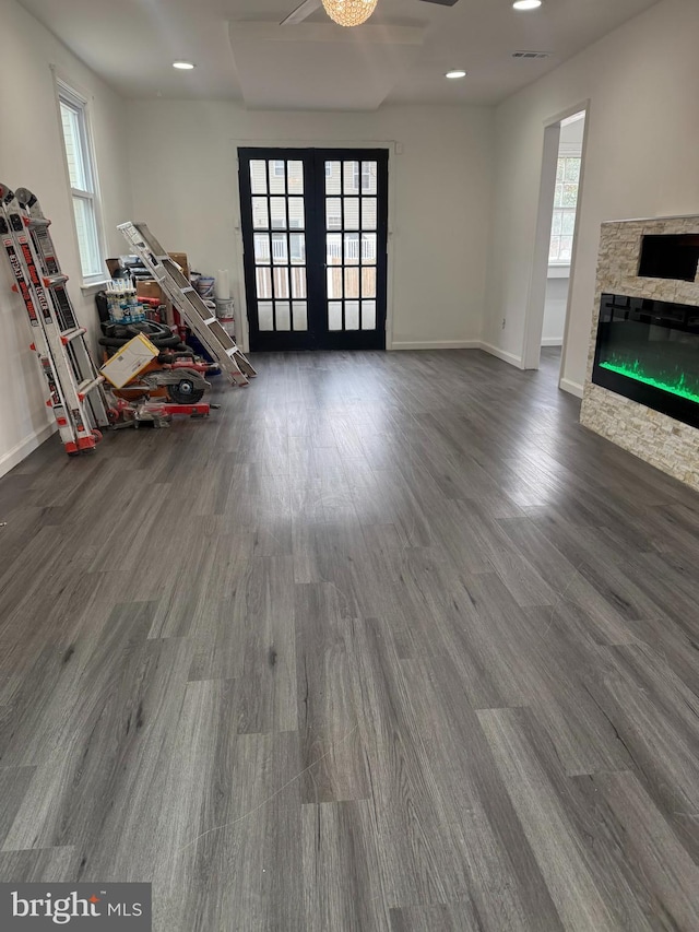 unfurnished living room featuring dark wood-type flooring, french doors, a wealth of natural light, and a stone fireplace