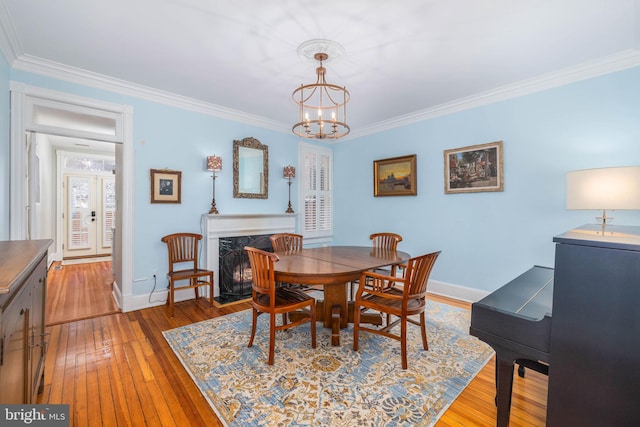 dining room with a fireplace, light hardwood / wood-style flooring, ornamental molding, and a notable chandelier