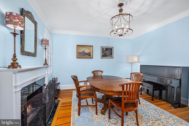 dining space with crown molding, a fireplace, a chandelier, and hardwood / wood-style flooring