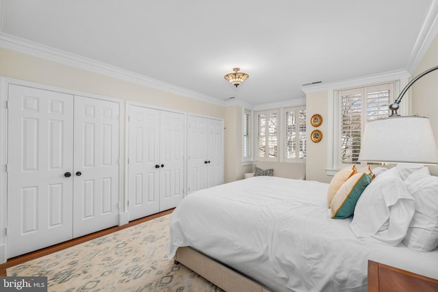 bedroom featuring hardwood / wood-style floors, multiple closets, and crown molding