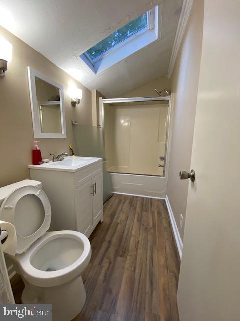 full bathroom with toilet, hardwood / wood-style flooring, shower / washtub combination, lofted ceiling with skylight, and vanity