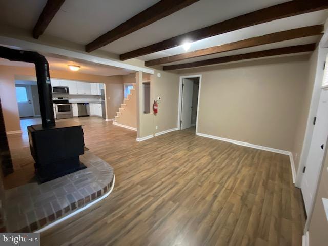 living room featuring a wood stove, beam ceiling, and hardwood / wood-style floors