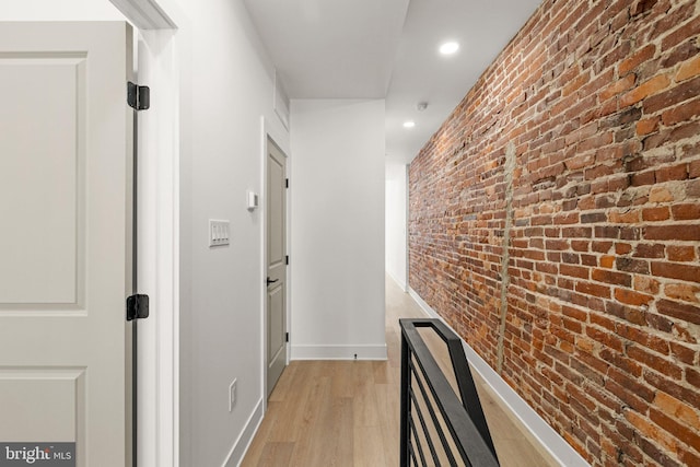 corridor featuring brick wall and light hardwood / wood-style flooring