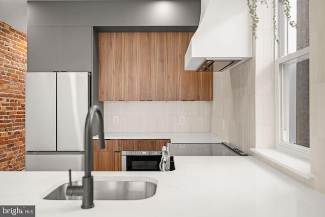 kitchen featuring stainless steel refrigerator, decorative backsplash, sink, and custom range hood