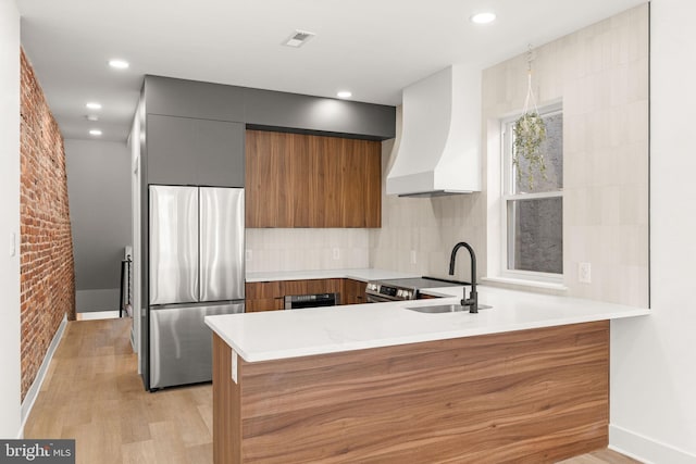 kitchen with sink, custom range hood, kitchen peninsula, stainless steel appliances, and brick wall