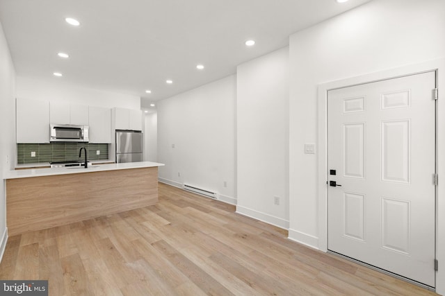 kitchen with backsplash, stainless steel appliances, baseboard heating, sink, and white cabinetry