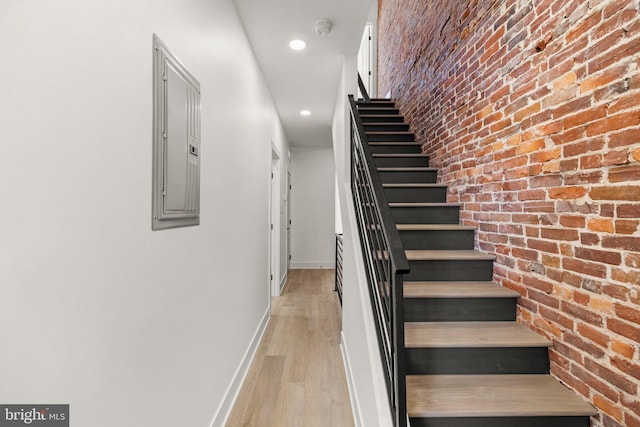 staircase featuring electric panel, brick wall, and hardwood / wood-style flooring