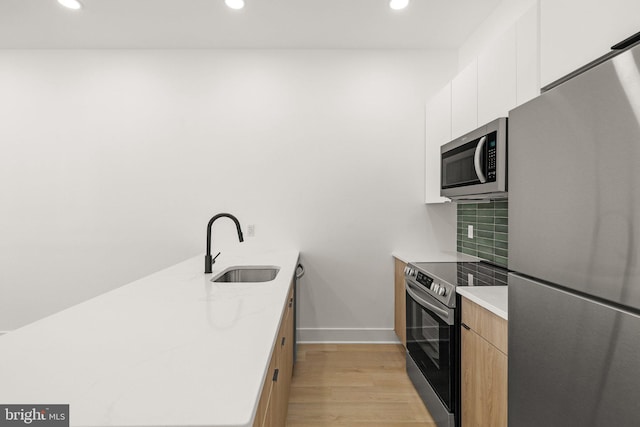 kitchen with backsplash, white cabinets, sink, light hardwood / wood-style floors, and stainless steel appliances