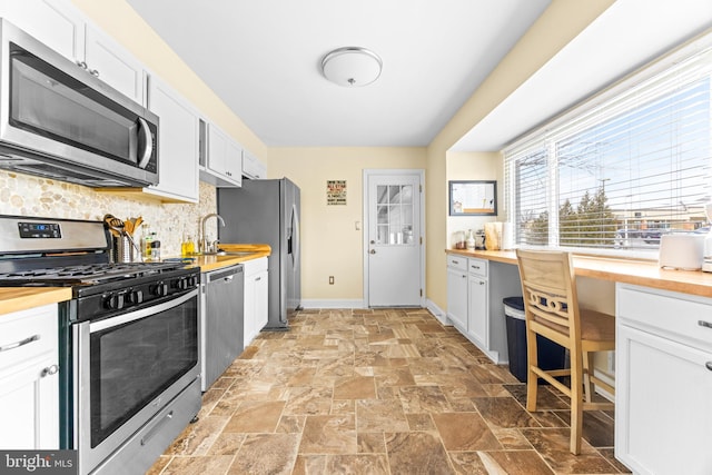 kitchen with appliances with stainless steel finishes, tasteful backsplash, white cabinetry, and butcher block counters