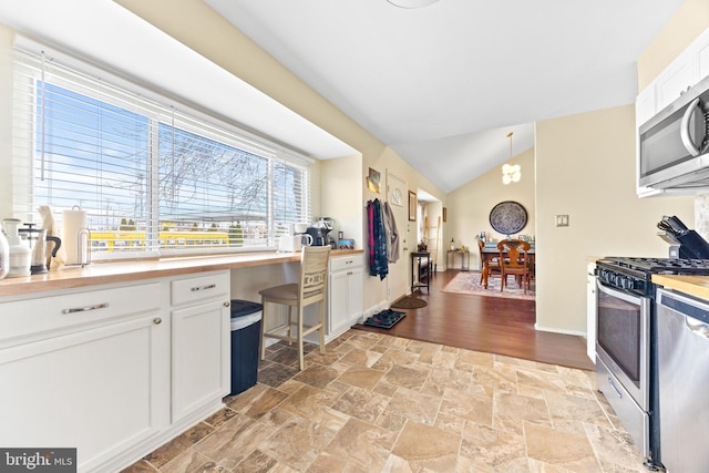 kitchen with appliances with stainless steel finishes, vaulted ceiling, pendant lighting, a notable chandelier, and white cabinetry