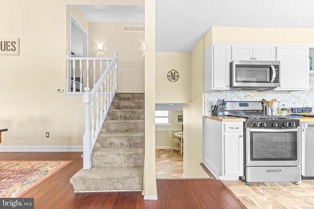 kitchen featuring decorative backsplash, white cabinetry, hardwood / wood-style floors, and appliances with stainless steel finishes