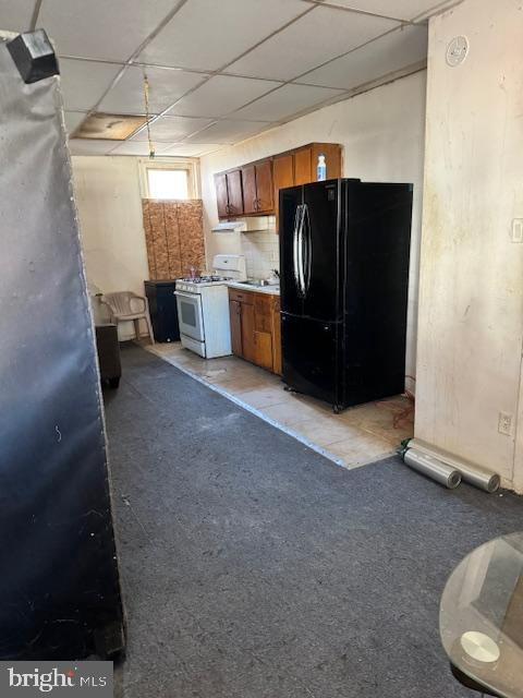 kitchen featuring white range with gas cooktop, decorative backsplash, and black refrigerator