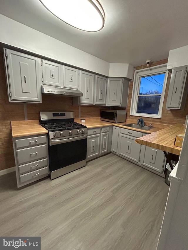 kitchen featuring light wood-type flooring, stainless steel appliances, gray cabinets, butcher block counters, and range hood