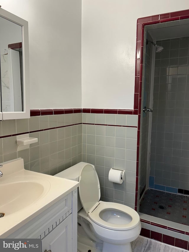 bathroom with vanity, toilet, a tile shower, and tile walls