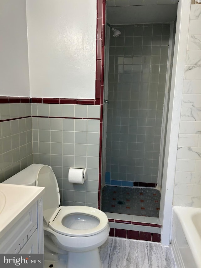 bathroom with a tile shower, vanity, toilet, and tile walls