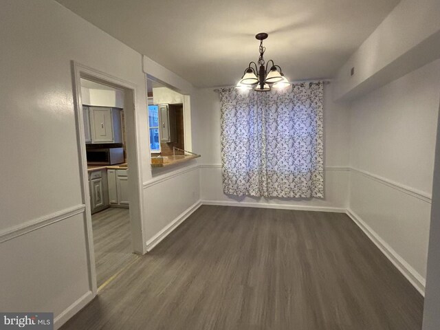 unfurnished dining area featuring an inviting chandelier and dark wood-type flooring