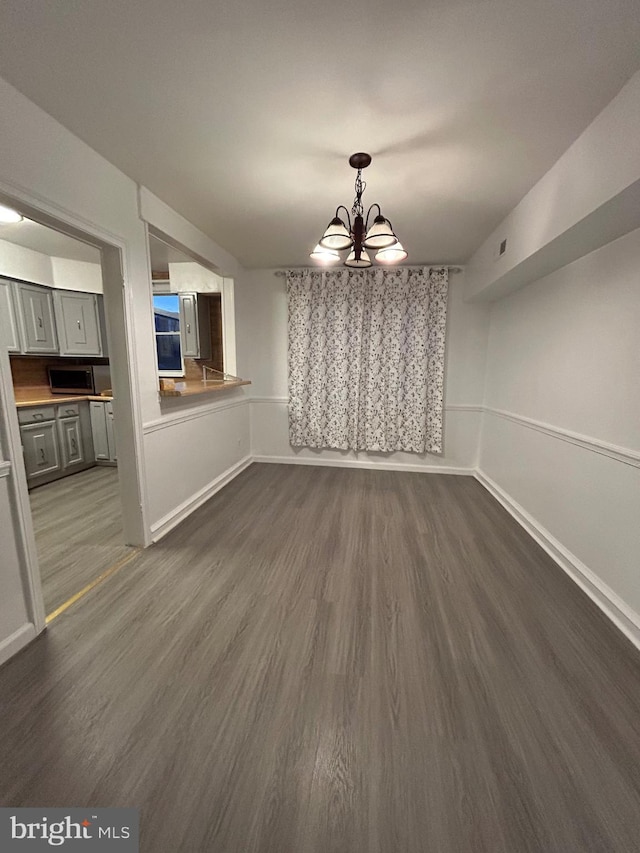 unfurnished dining area featuring dark hardwood / wood-style floors and an inviting chandelier