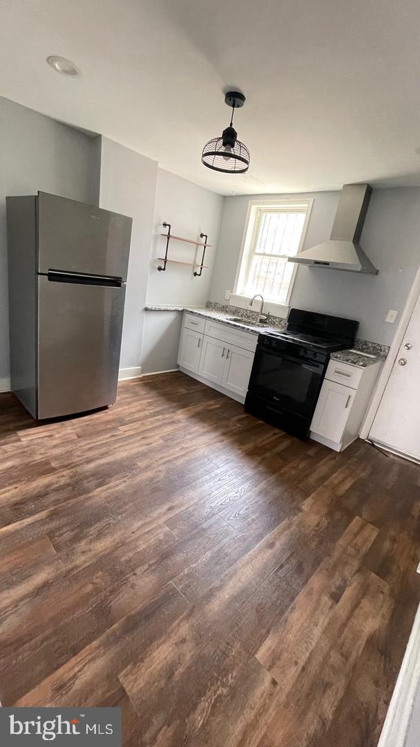 kitchen with white cabinetry, sink, wall chimney exhaust hood, black range oven, and stainless steel fridge