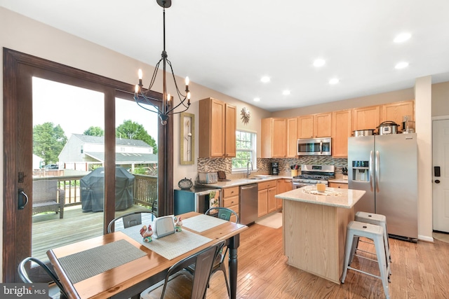 kitchen with appliances with stainless steel finishes, sink, a notable chandelier, a kitchen island, and hanging light fixtures