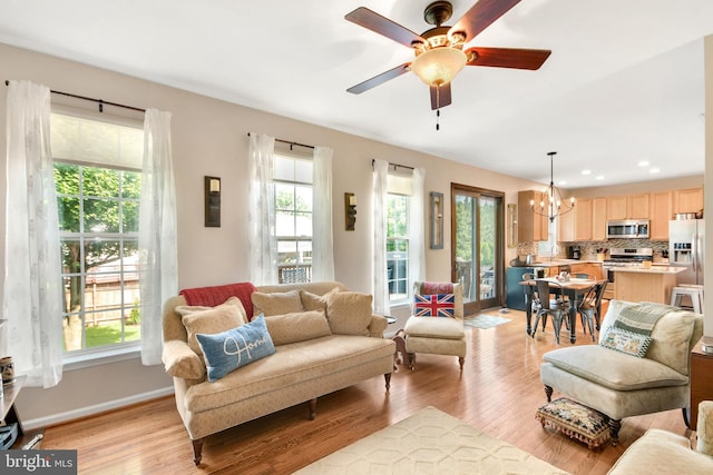 living room with a healthy amount of sunlight, light hardwood / wood-style floors, and ceiling fan with notable chandelier