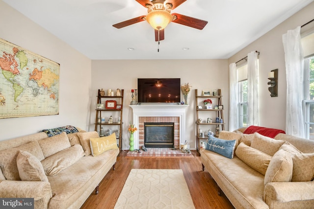 living room with ceiling fan, wood-type flooring, and a brick fireplace