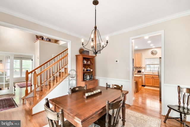 dining area with light hardwood / wood-style flooring, ornamental molding, sink, and an inviting chandelier