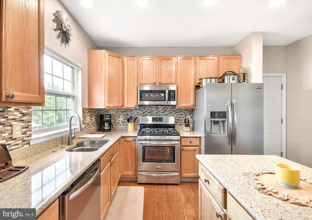 kitchen with sink, light wood-type flooring, appliances with stainless steel finishes, tasteful backsplash, and light stone counters