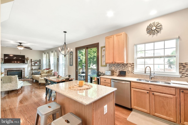 kitchen with sink, stainless steel dishwasher, decorative backsplash, a kitchen island, and ceiling fan with notable chandelier