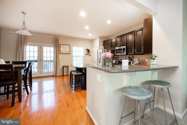 kitchen with pendant lighting, light hardwood / wood-style flooring, appliances with stainless steel finishes, a kitchen bar, and kitchen peninsula