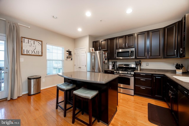 kitchen with a center island, a kitchen breakfast bar, sink, light wood-type flooring, and stainless steel appliances