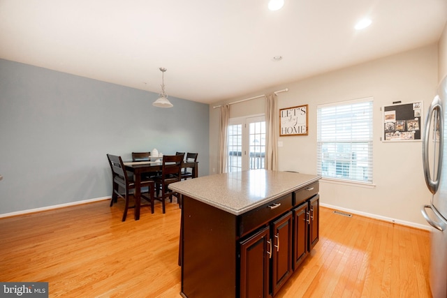 kitchen with decorative light fixtures, a kitchen island, stainless steel refrigerator, and light hardwood / wood-style flooring