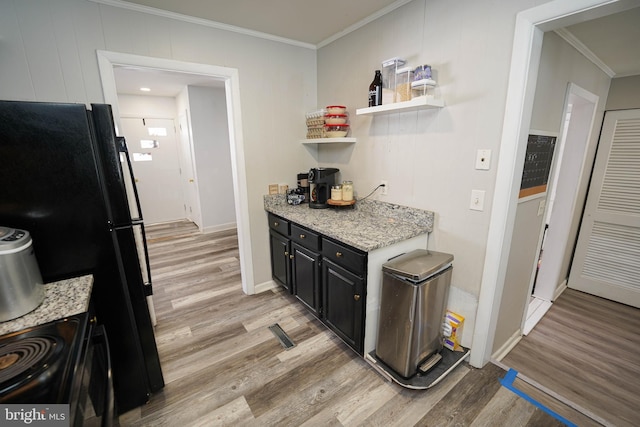 kitchen with black fridge, light stone counters, ornamental molding, light wood-type flooring, and range