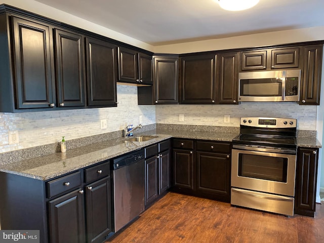 kitchen featuring appliances with stainless steel finishes, dark hardwood / wood-style flooring, tasteful backsplash, sink, and stone countertops