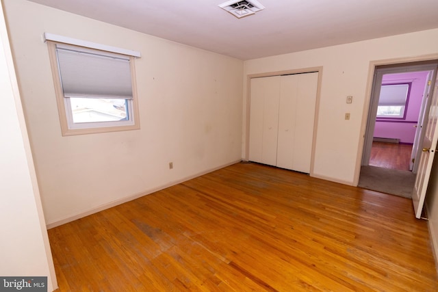 unfurnished bedroom featuring light wood-type flooring, baseboard heating, and a closet