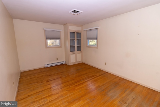 unfurnished room with light hardwood / wood-style floors, a healthy amount of sunlight, and a baseboard heating unit