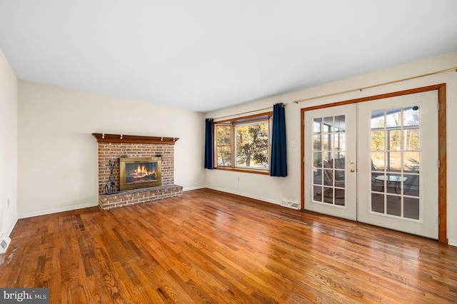 unfurnished living room with a brick fireplace, hardwood / wood-style flooring, and french doors